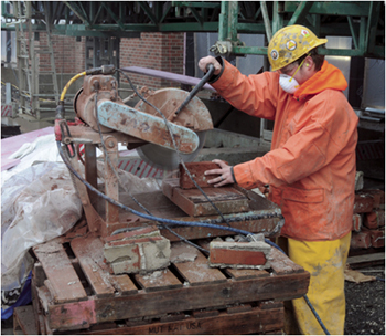 This is a picture of a worker wearing a mask while cutting bricks with a saw