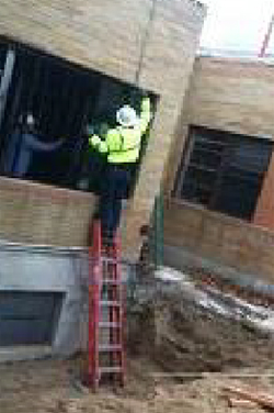 Worker using a stepladder improperly by standing on its top
step with the ladder propped against the building in its closed position.